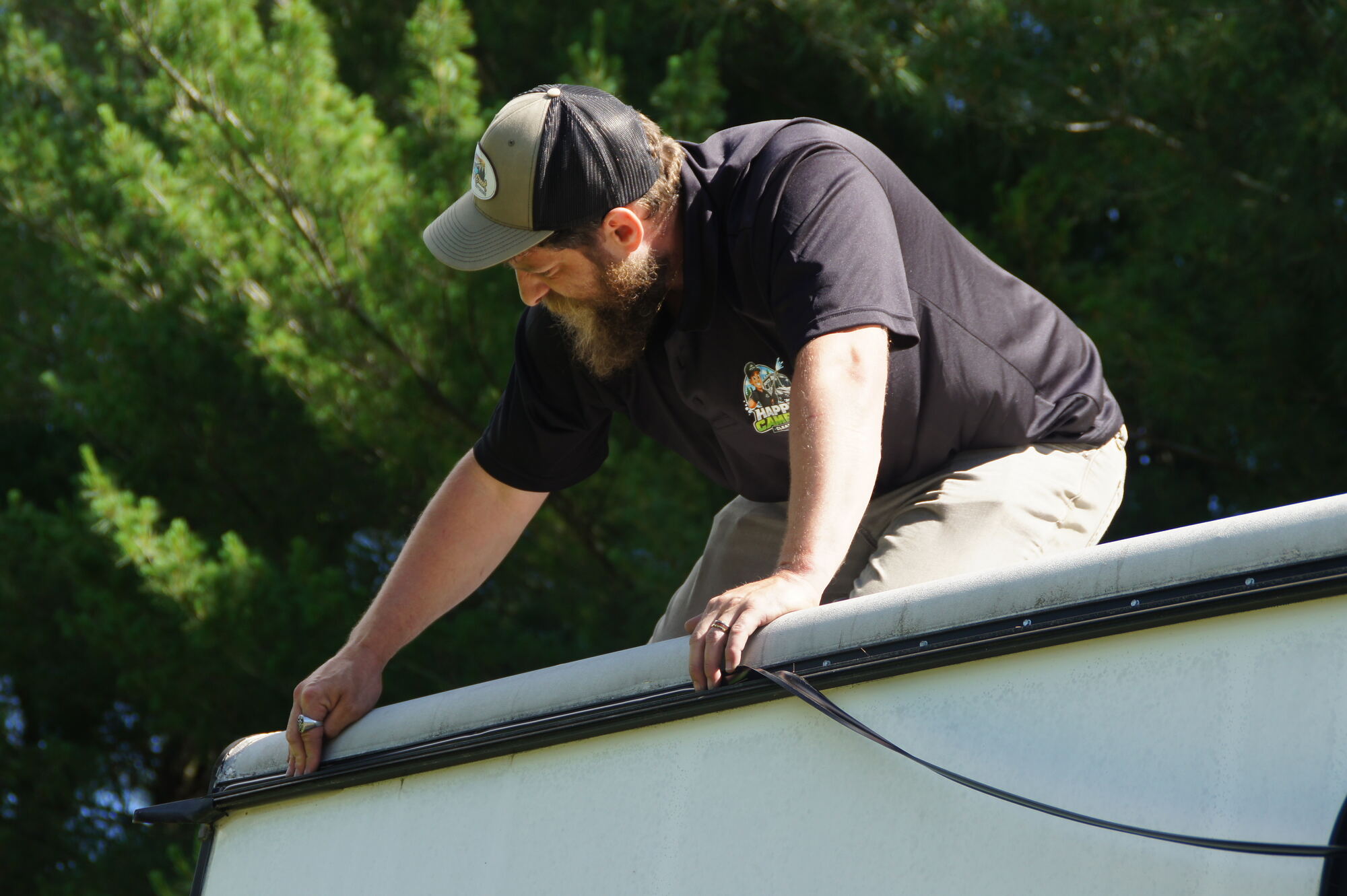 Happy Camper Clean & Fix technician on an RV roof sealing a seam against the sky
